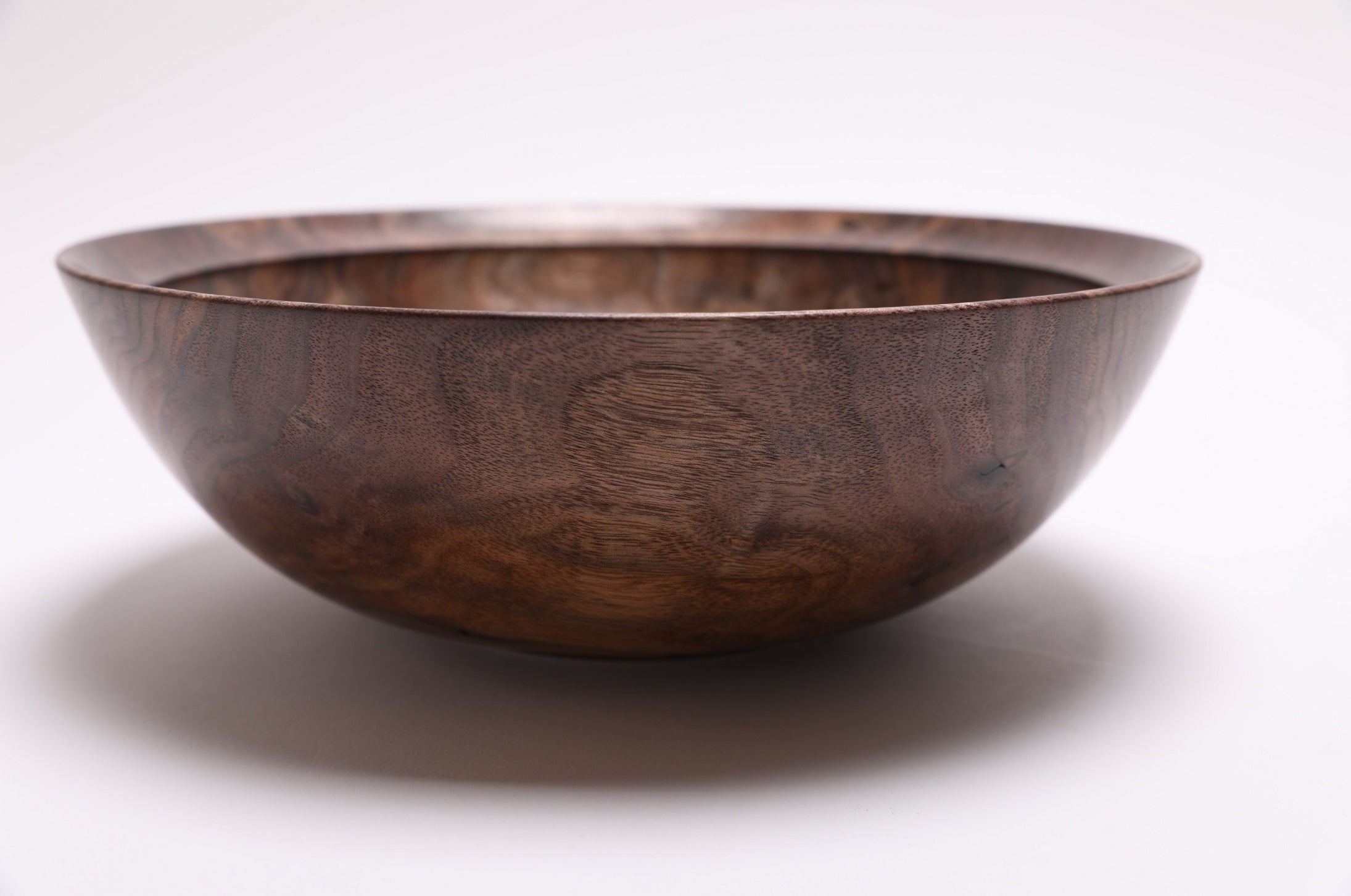 Handmade curly walnut bowl angle view displaying undercut rim and raised foot design