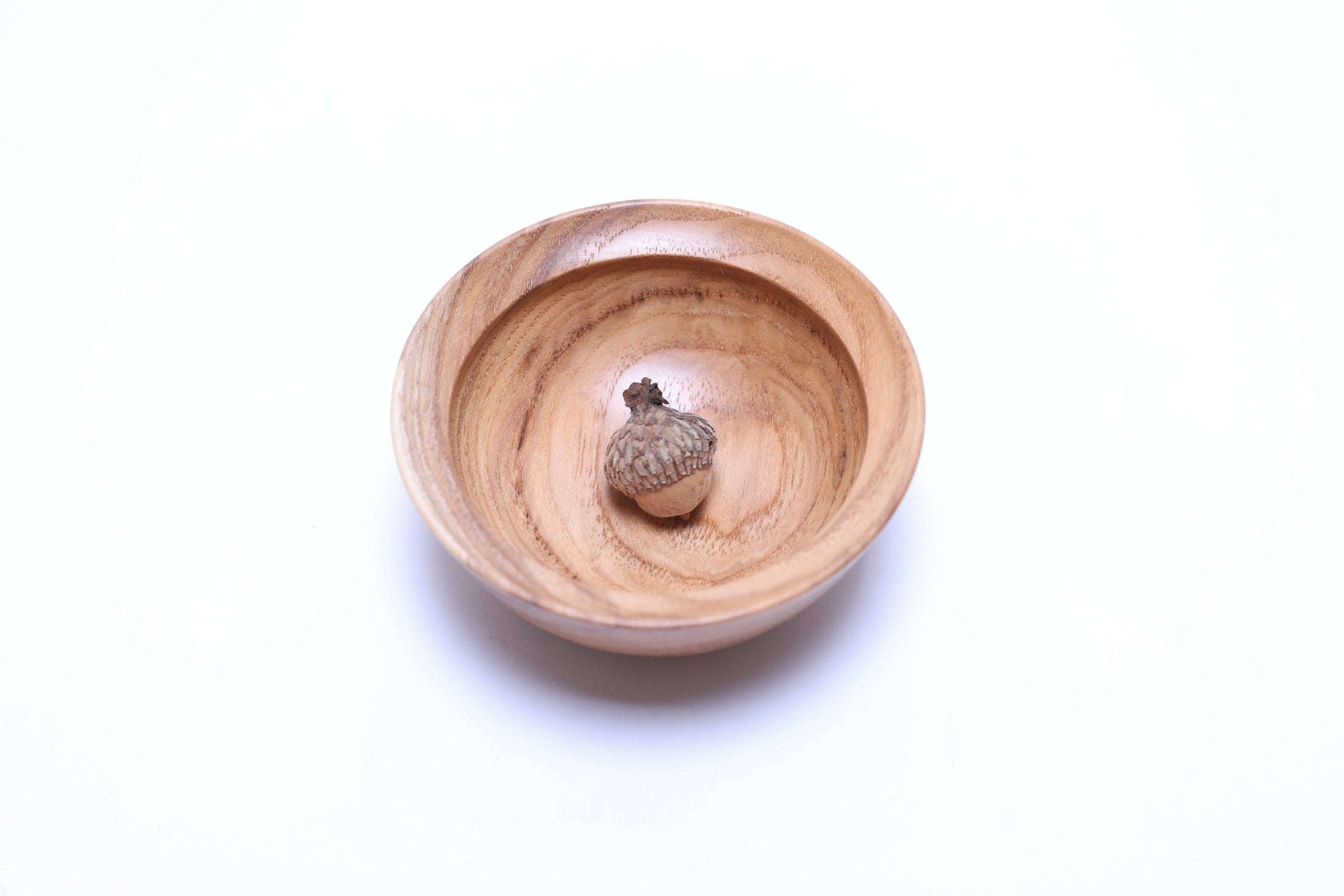 Hickory wood bowl side profile highlighting rounded curved taper and raised foot with acorn in the bowl.