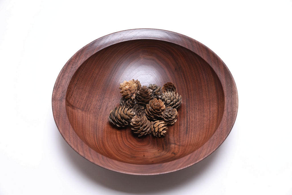 Handmade walnut bowl with mini pine cones displaying undercut rim and raised foot design
