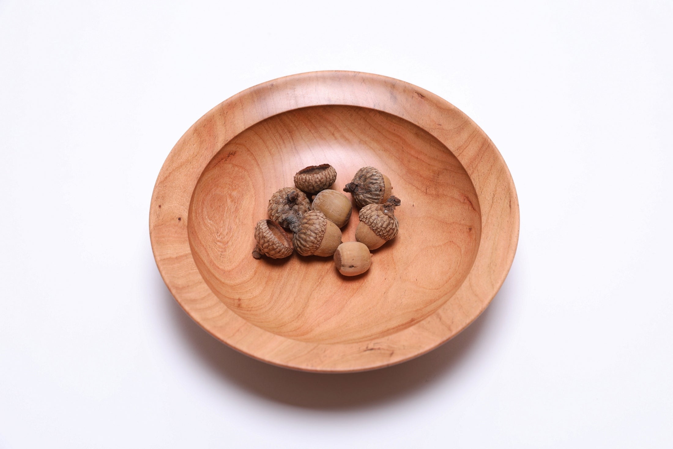 Handmade cherry wooden bowl, overhead view showing pink and copper color variation ad acorns in the bottom of the bowl