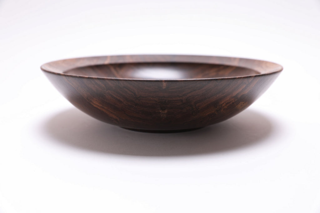 Curly wild black walnut wooden bowl side view rotated 180 degrees — raised foot and smooth underside, warm milk chocolate and gray tones with natural oil finish