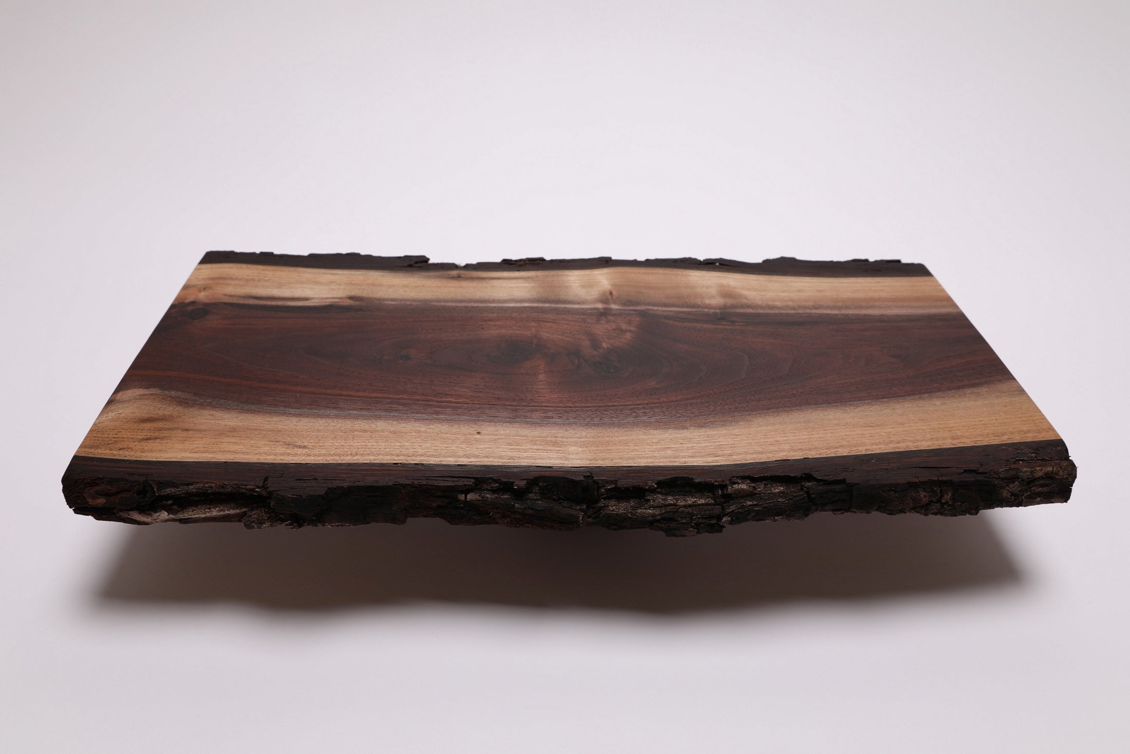 A rectangular live-edge black walnut wooden serving/charcuterie board with a natural bark border, showcasing dark and light wood grain patterns, photographed against a neutral light gray background.