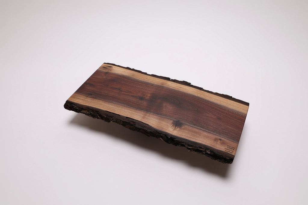 A rectangular live-edge black walnut wooden serving board with a natural bark border, displayed on a clean white background.