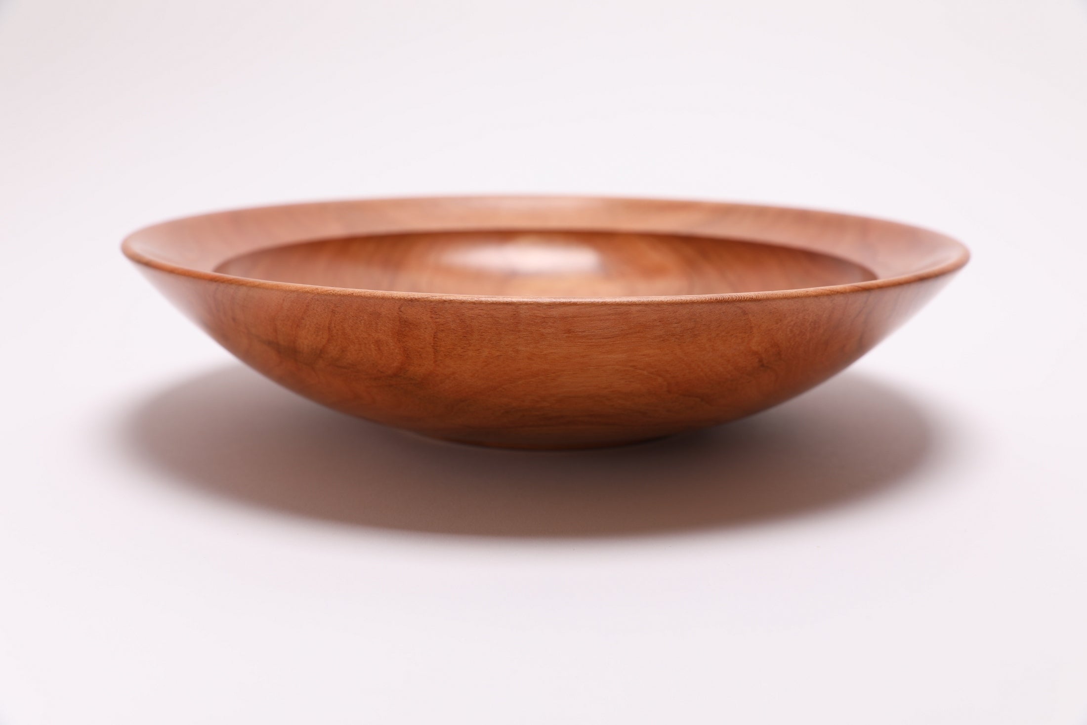 Side view of handcrafted wild black cherry wooden bowl showing curved taper, undercut rim, and raised foot