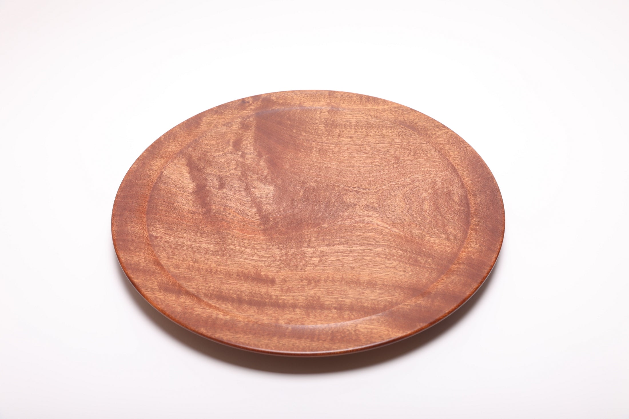 Large Khaya serving platter top view rotated 60°, iridescent African mahogany grain in natural light