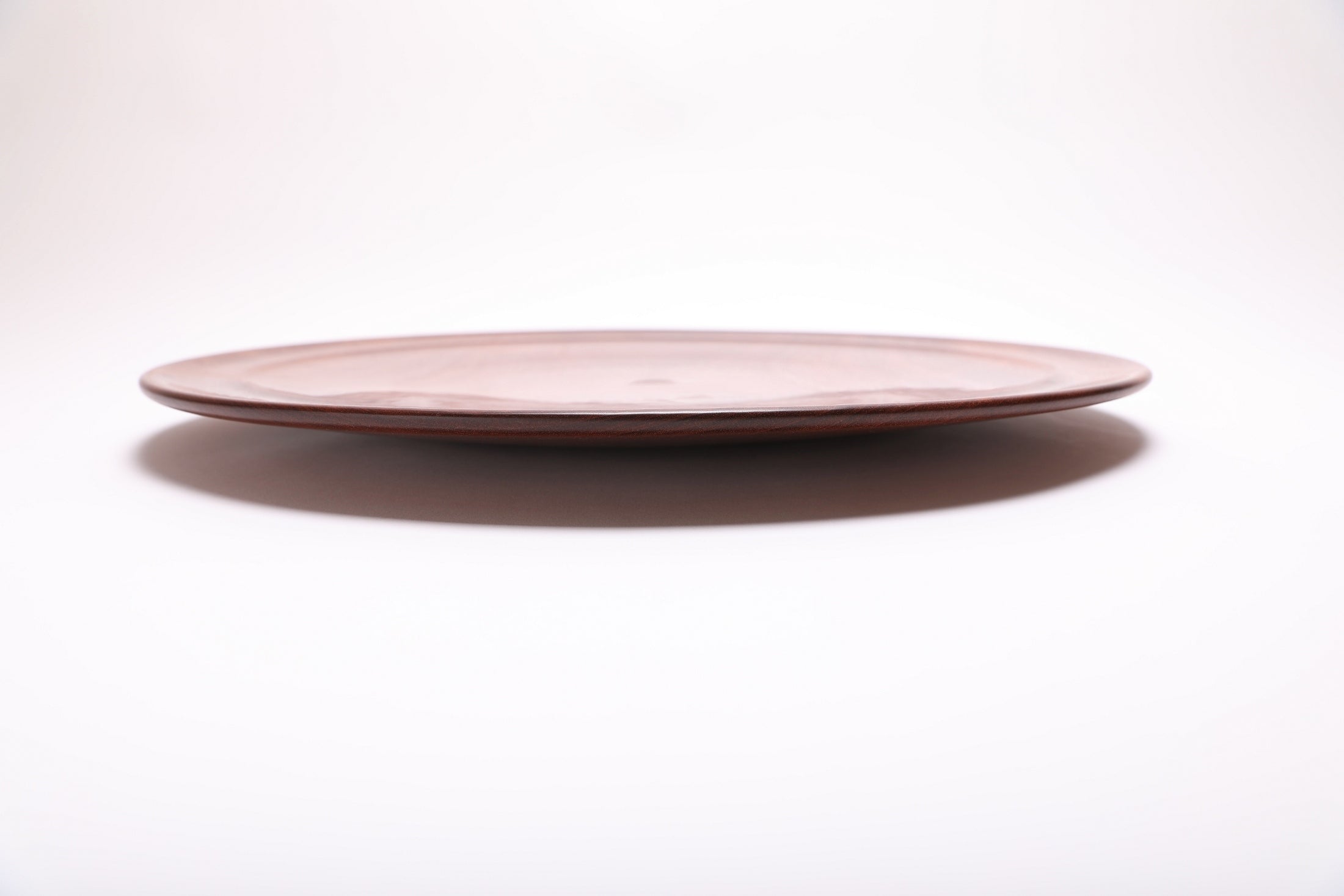 Side view of handcrafted large Khaya serving platter showing curved taper, undercut rim, and raised foot – 1 1/4" depth