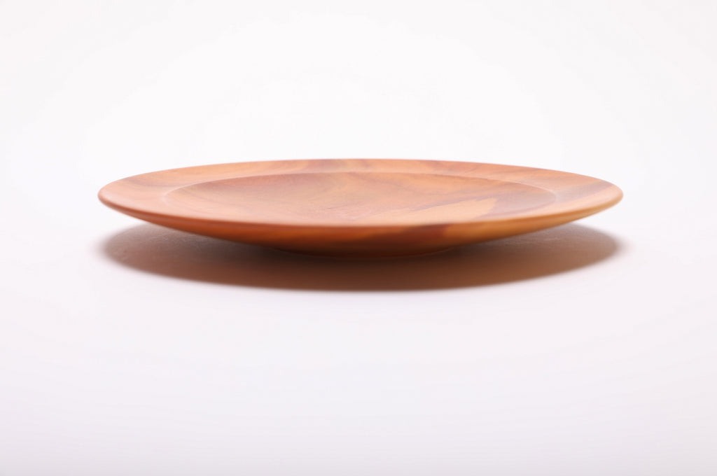 Side profile of pink ivory wooden dish showing curved taper, undercut rim, raised foot, and shallow elegant form