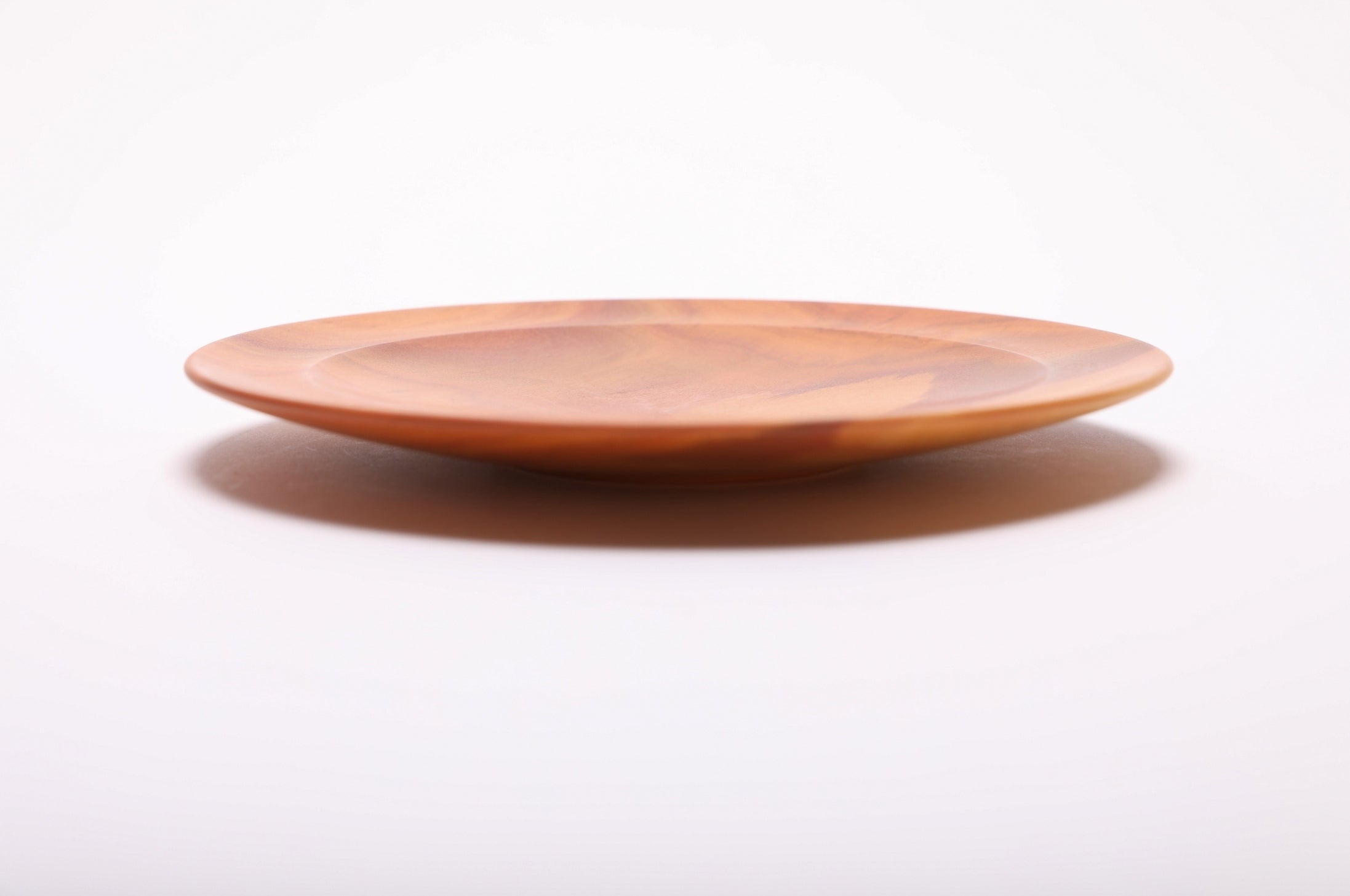 Side profile of pink ivory wooden dish showing curved taper, undercut rim, raised foot, and shallow elegant form