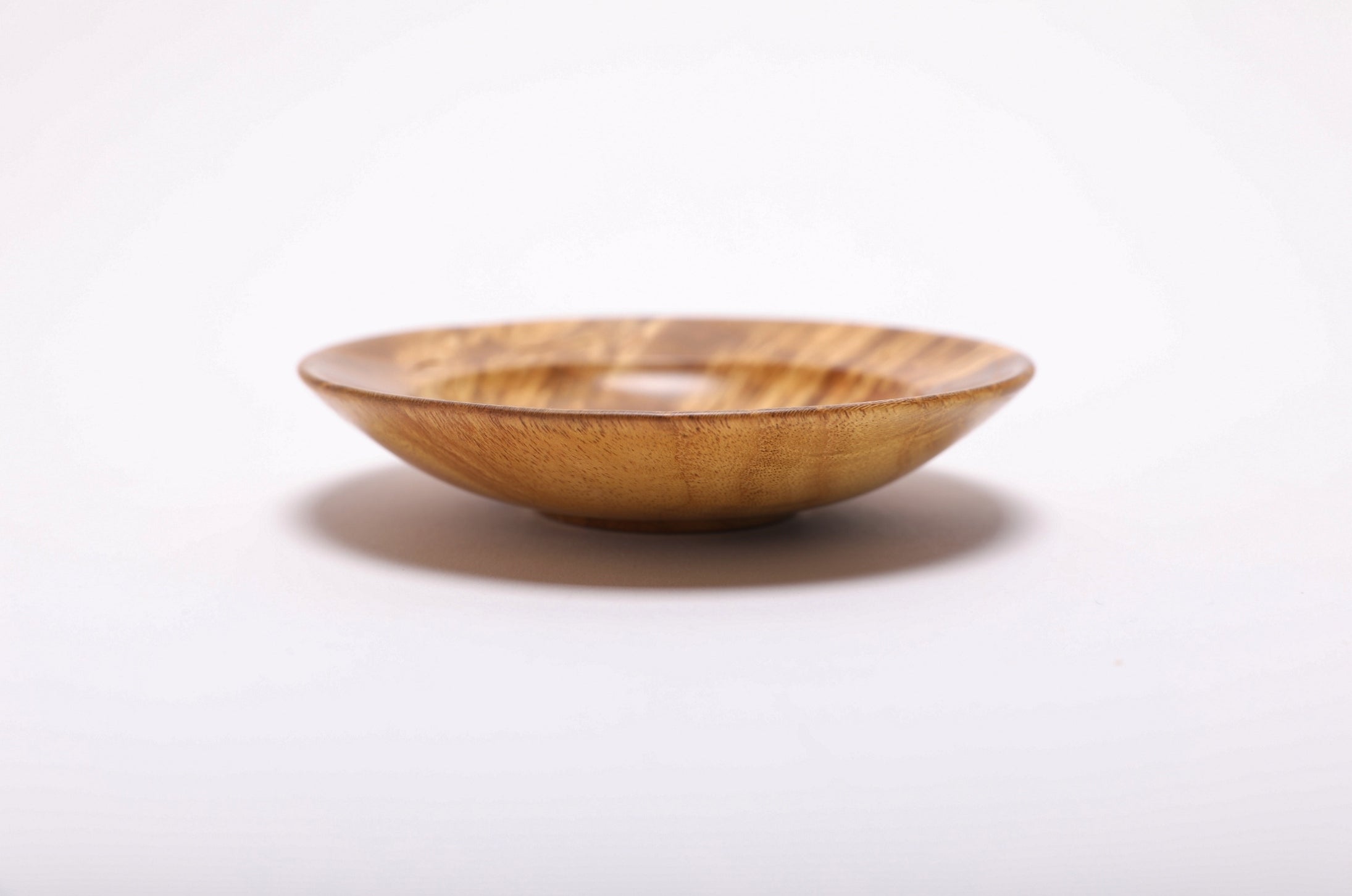 Side angle of mulberry burl ring dish highlighting small raised foot detail and smooth curved taper form