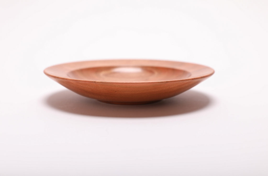 Side view of quartersawn wild black cherry ring dish showing rounded rim, curved taper, undercut edge, and raised foot, handmade in NC USA