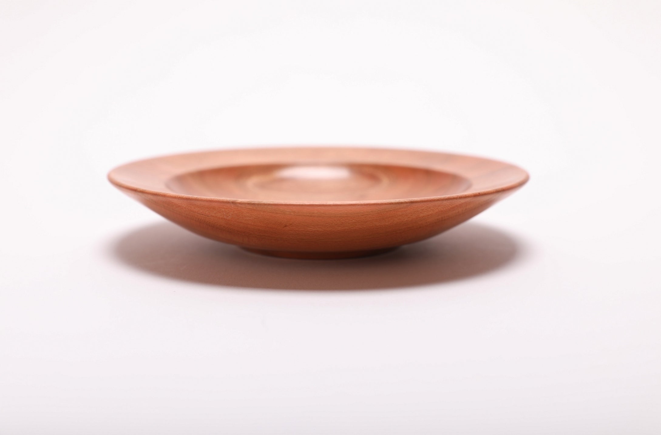 Side view of quartersawn wild black cherry ring dish showing rounded rim, curved taper, undercut edge, and raised foot, handmade in NC USA