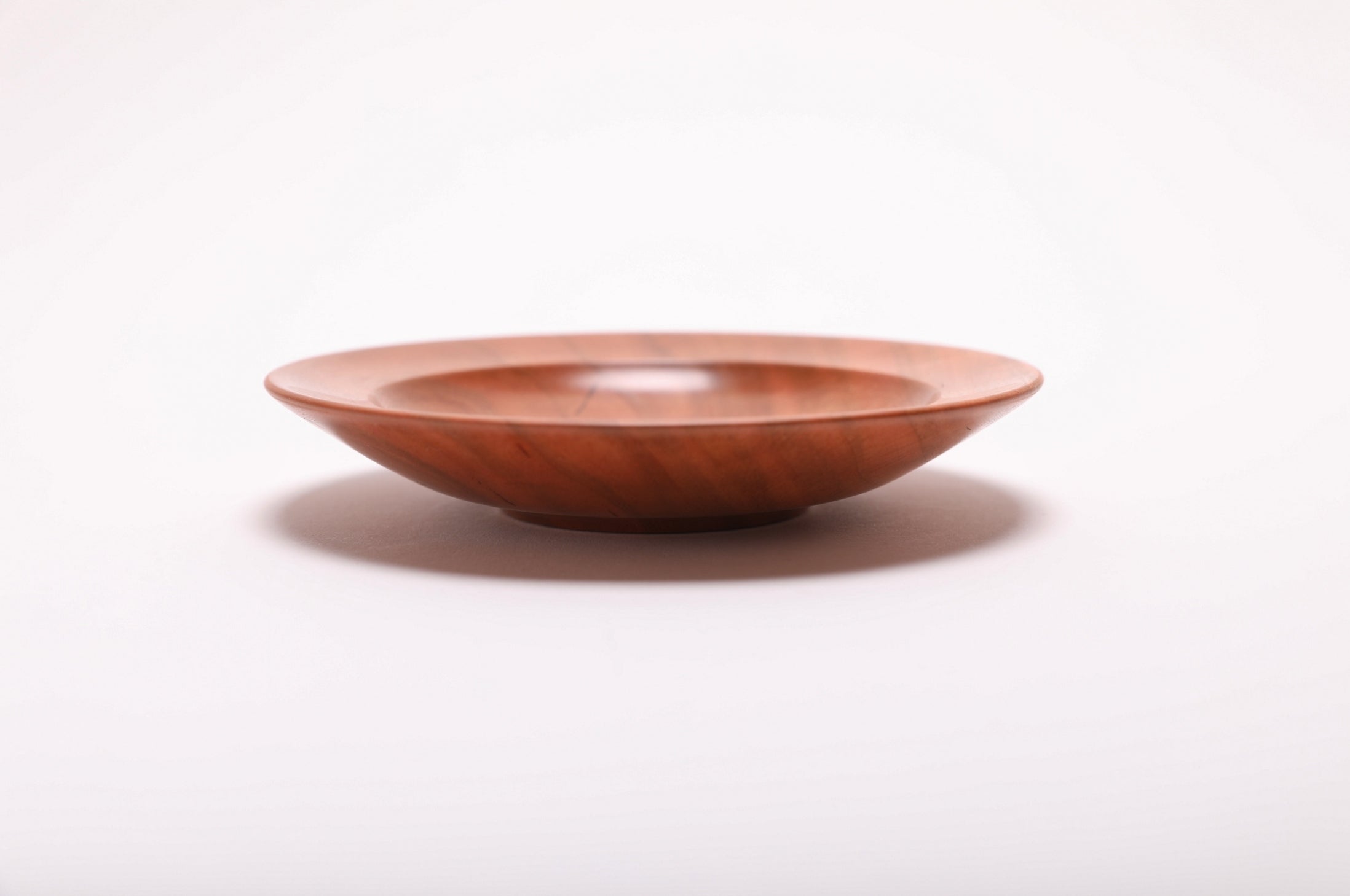 Side angle of wild black cherry ring dish rotated 270 degrees highlighting raised foot detail and smooth curved taper