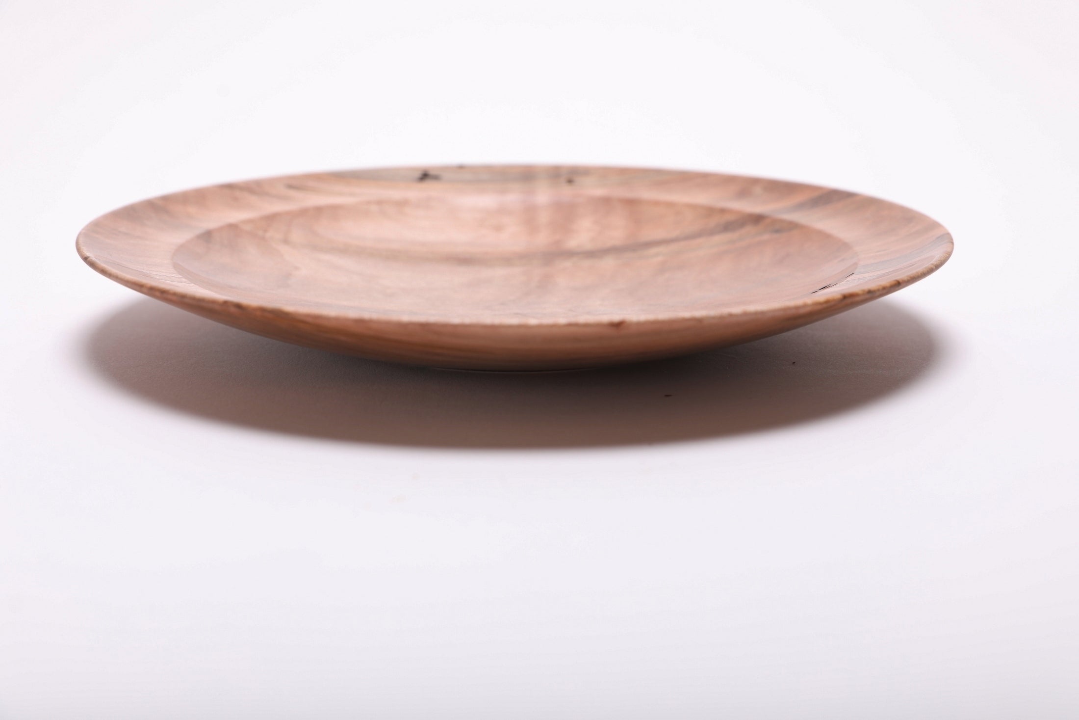 Side angle of ambrosia maple shallow plate rotated 270 degrees highlighting raised foot detail and graceful low-profile form