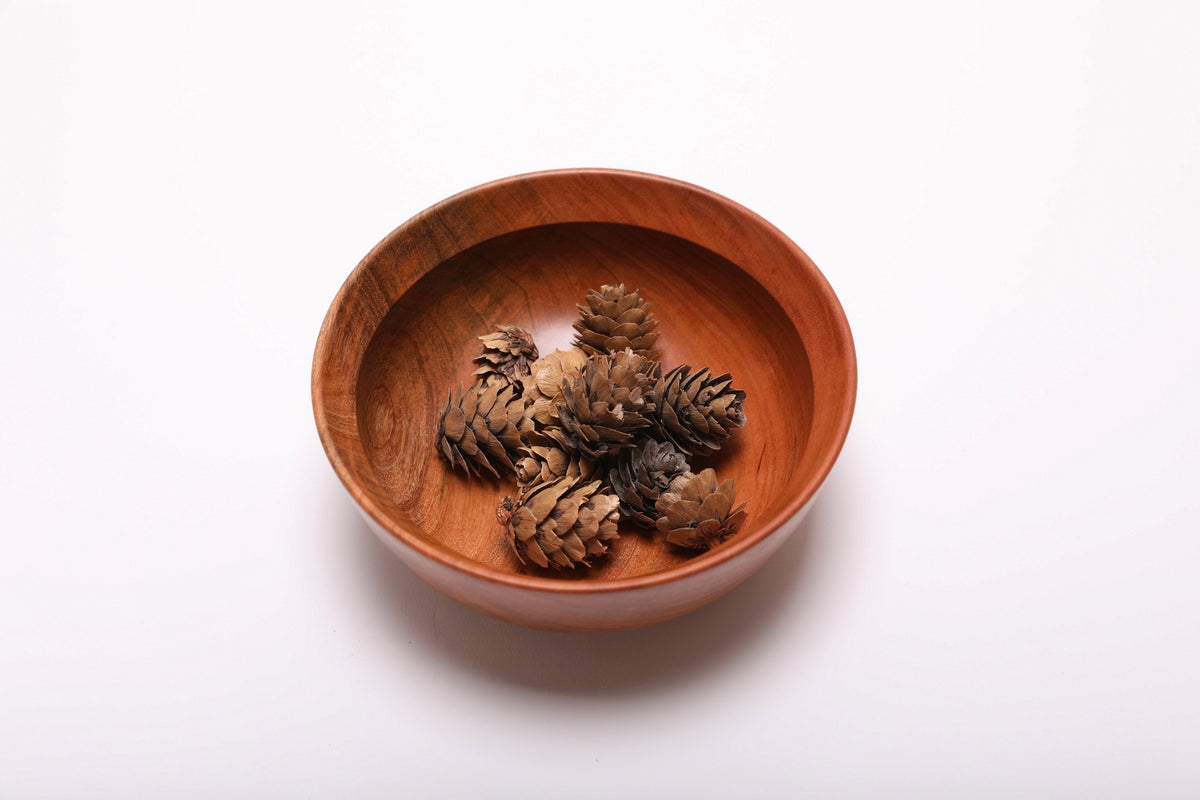 Hand-turned black cherry wood bowl with mini pine cones, showing scale and natural finish