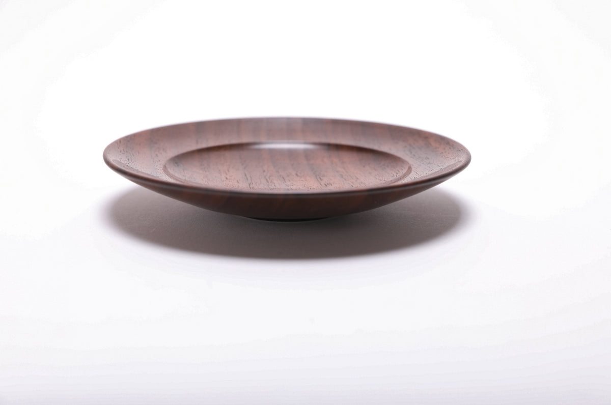 Side view of hand-turned black walnut wooden ring dish showing reddish-brown highlights and raised foot detail