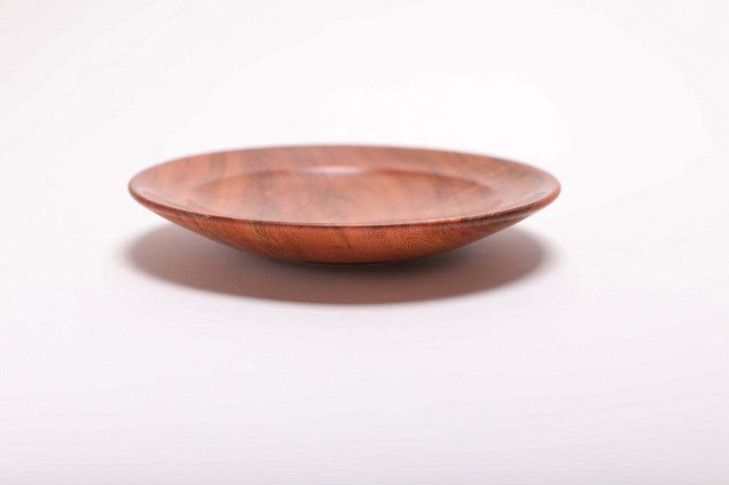 Side view of hand-turned black cherry burl ring dish showing raised foot and deep pink-orange wood coloration