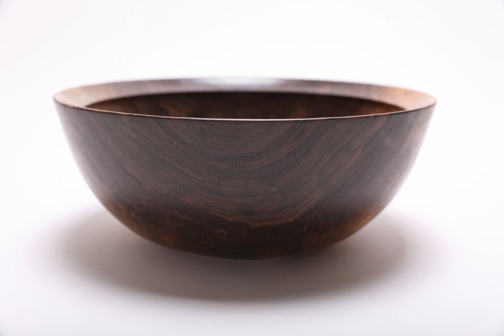 Side view of hand-turned spalted black walnut bowl showing bud scar detail and deep curved profile with raised foot