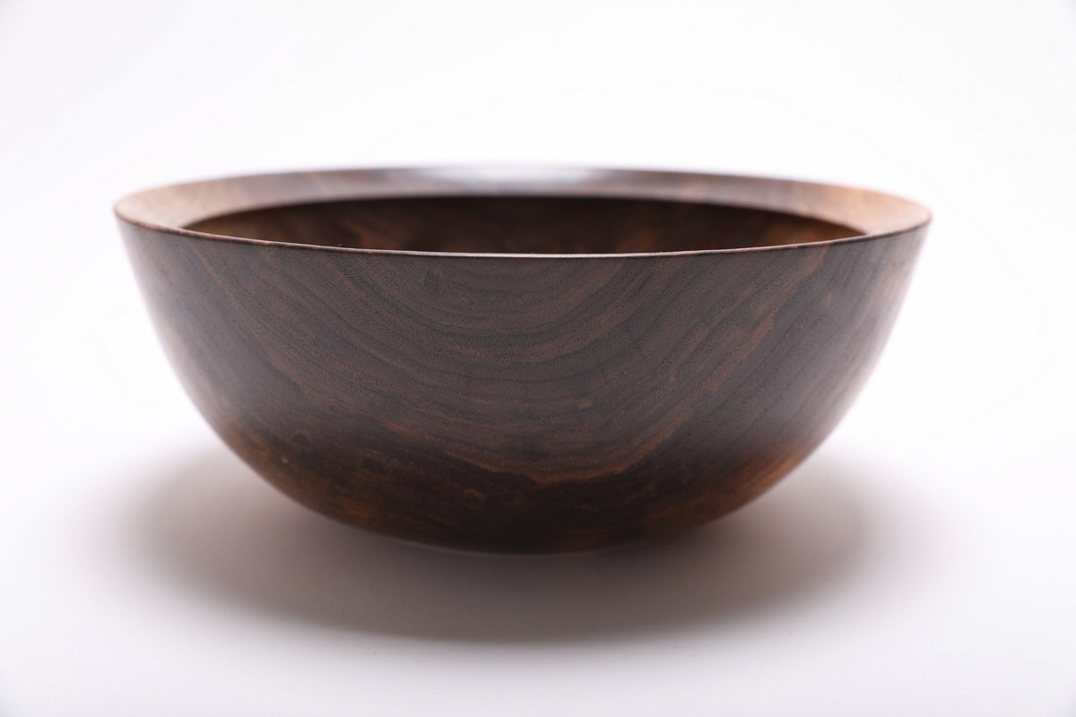 Side view of hand-turned spalted black walnut bowl showing bud scar detail and deep curved profile with raised foot