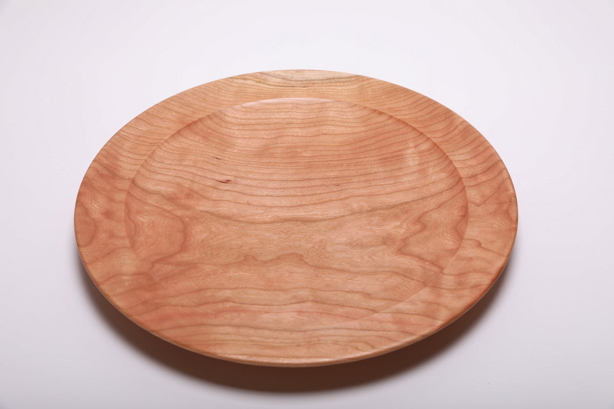 Top view of hand-turned curly wild black cherry wooden platter showing warm salmon-pink grain with curly figure and concentric growth ring lines, 15 inches