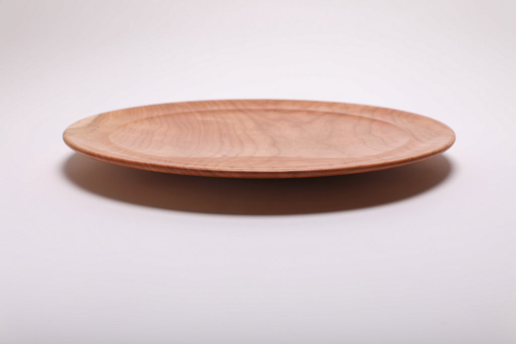 Side profile of hand-turned curly wild black cherry wooden platter showing thin curved taper, raised foot, and warm pink-toned exterior, 1 1/2 inch height