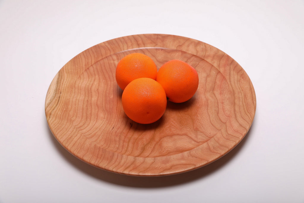 Three oranges resting on a hand-turned curly wild black cherry platter for scale, top view, 15 inch diameter