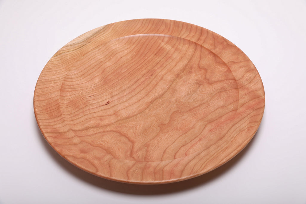 Top view of hand-turned curly wild black cherry wooden platter showing flowing curly grain and warm salmon-pink tones with undercut rim, 15 inches