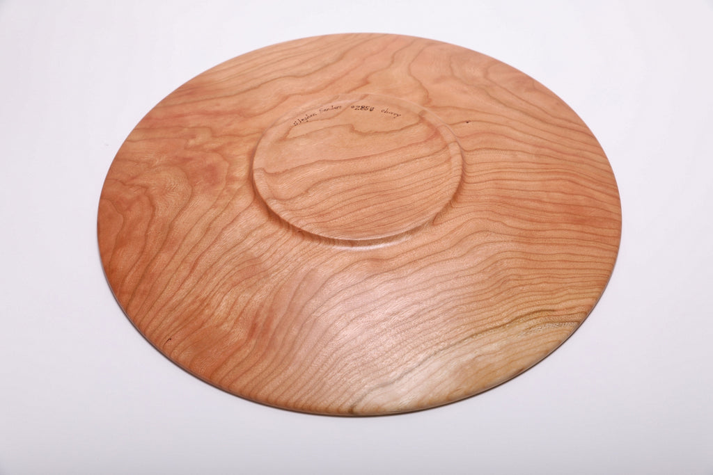 Bottom view of handmade curly wild black cherry wooden platter showing raised foot, curly grain, and maker's signature