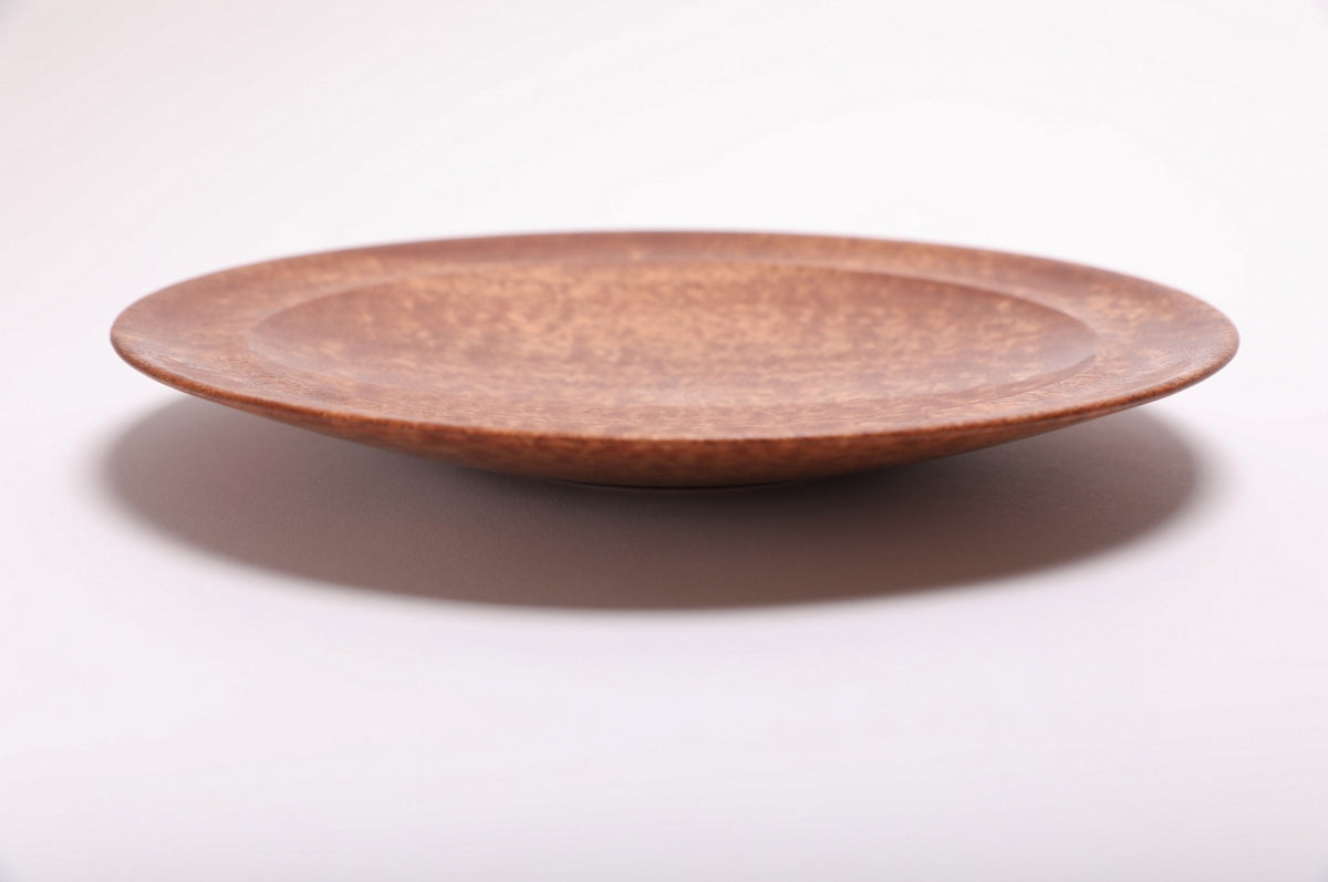 Side profile of hand-turned pommele sapele wooden bowl showing shallow curved form, raised foot, and rich mahogany exterior grain, 1 1/4 inch height