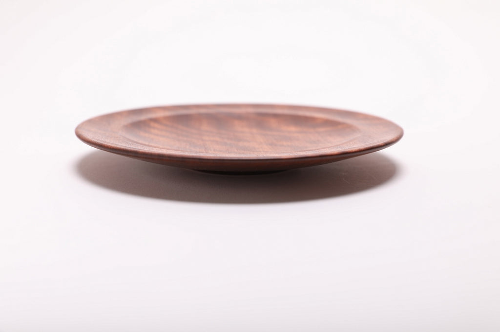 Side view of the sapele dish showing its curved taper, rounded rim, and raised foot