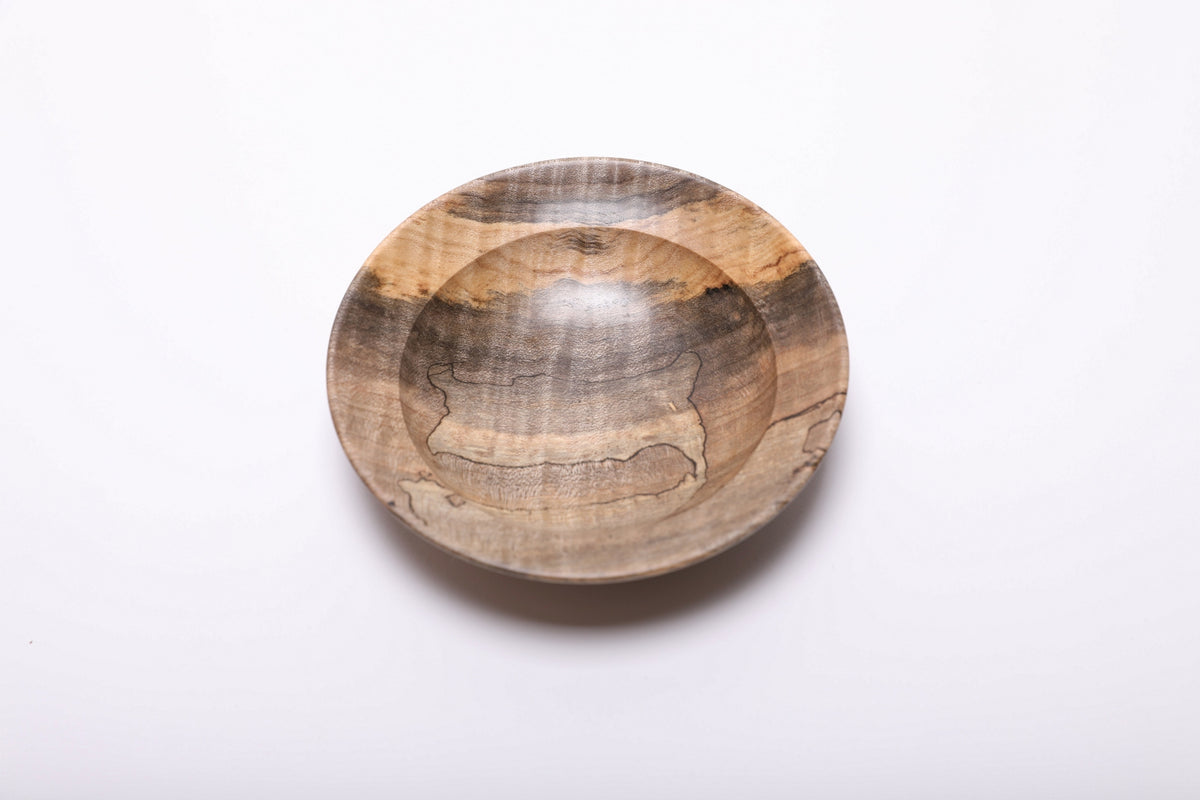 Spalted tiger maple dish viewed from above, showing dark figured grain across the center and a golden band along the far rim.