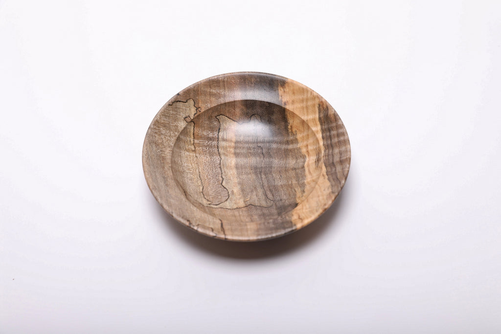 Top view of the wooden ring dish with golden maple along the right edge and irregular black lines across the gray-brown interior.
