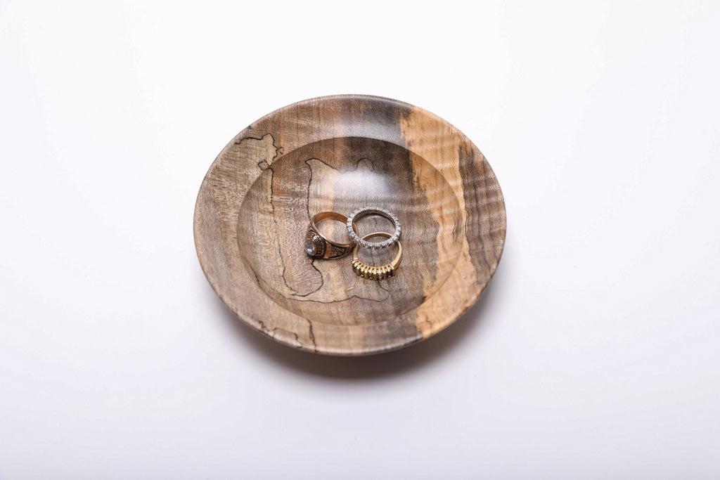 Spalted tiger maple ring dish holding three rings for scale, showing its shallow interior and broad rim. Rings not included.