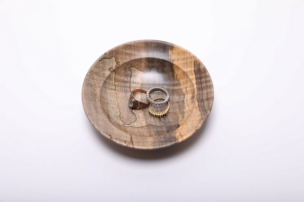Spalted tiger maple ring dish holding three rings for scale, showing its shallow interior and broad rim. Rings not included.