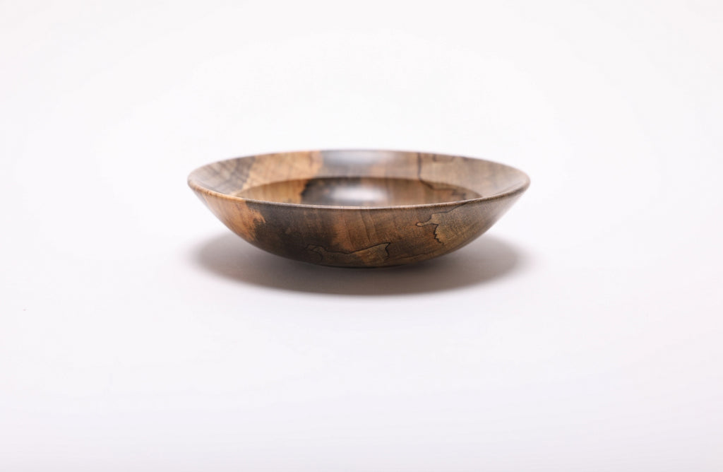 Maple ring dish viewed from the side, with black spalting lines across the curved wall and golden wood along the left edge.