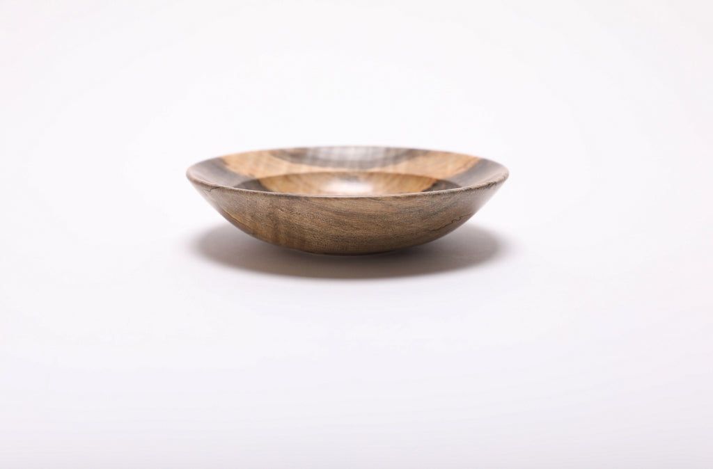 Side view of the wooden ring dish, showing its shallow shape, small raised foot and warm brown exterior grain.