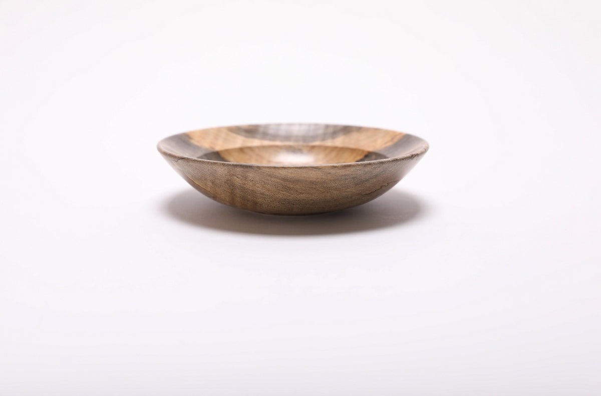 Side view of the wooden ring dish, showing its shallow shape, small raised foot and warm brown exterior grain.