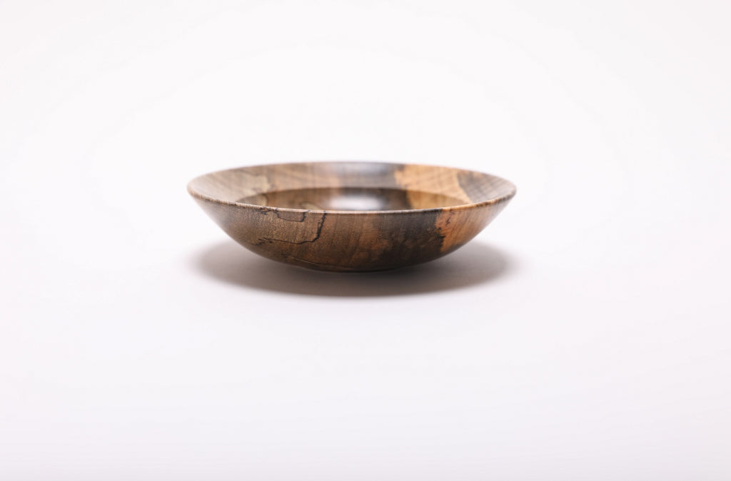 Spalted tiger maple ring dish from the side, with winding black lines on the left and contrasting dark and golden wood on the right.