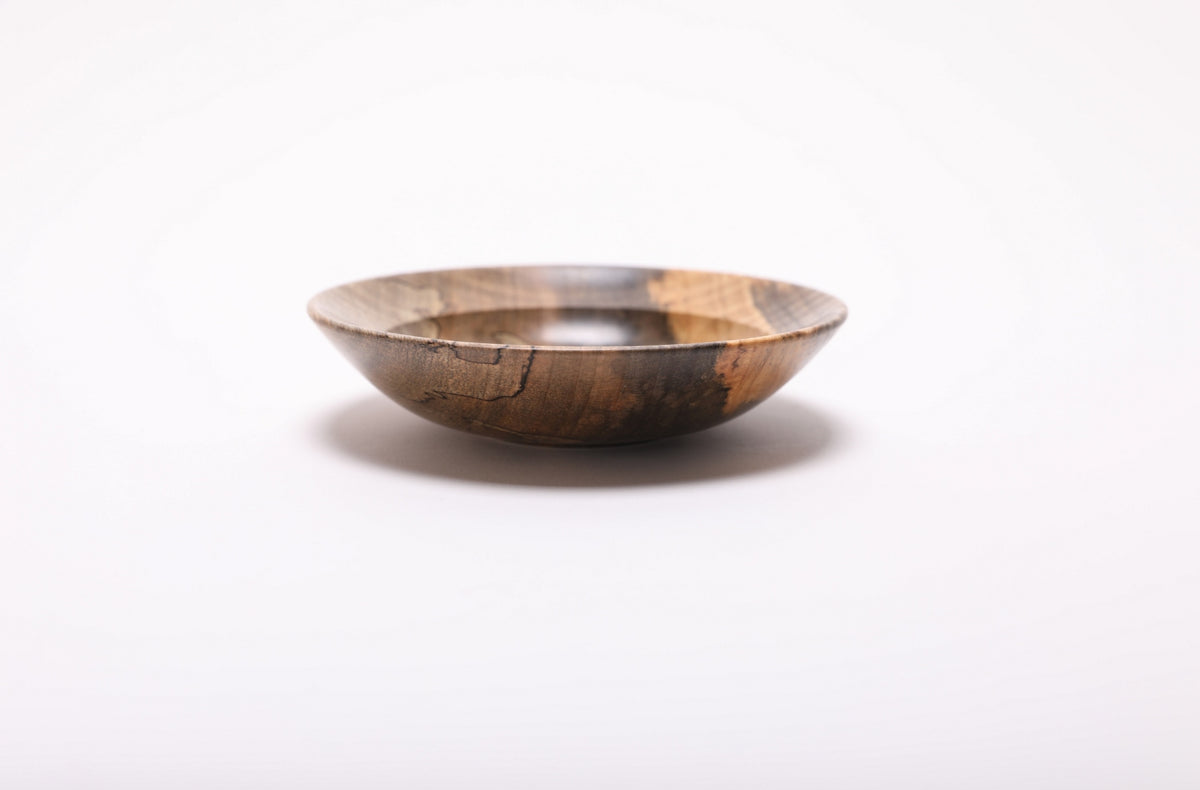 Spalted tiger maple ring dish from the side, with winding black lines on the left and contrasting dark and golden wood on the right.