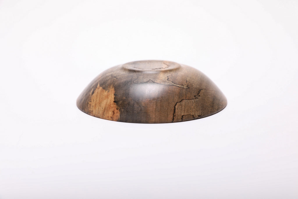 Underside view of the inverted maple ring dish, showing its raised circular foot, curved base and black spalting lines.