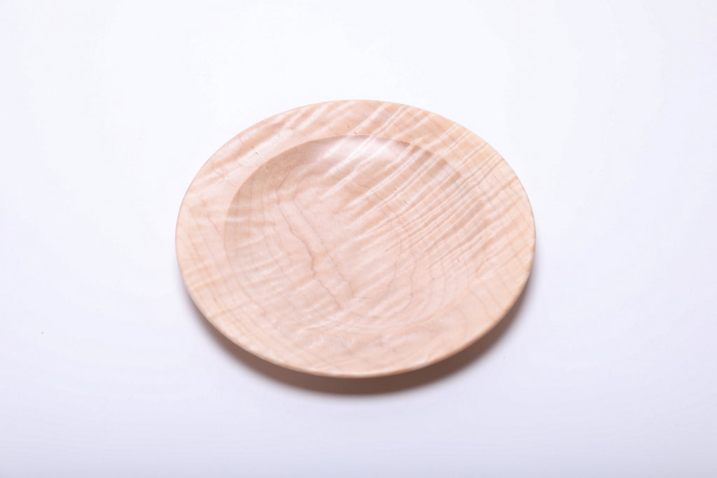 Tiger maple dish rotated to reveal diagonal highlights across its pale wooden surface and shallow center.