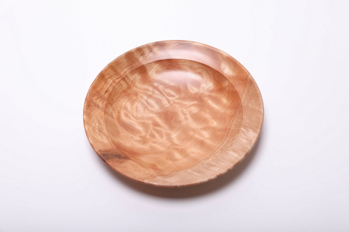 Top view showing cloudlike quilted figure across the maple dish and a darker grain marking on the lower left rim.