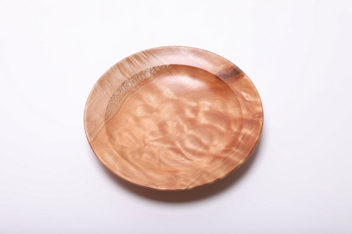 Top view of the maple dish with golden quilted grain, a gently recessed center, and a dark accent at the upper right edge.