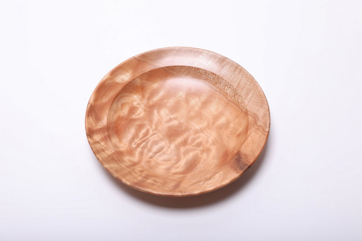 Maple ring dish from above, showing curling ribbons of light grain and a darker marking on the lower right rim.