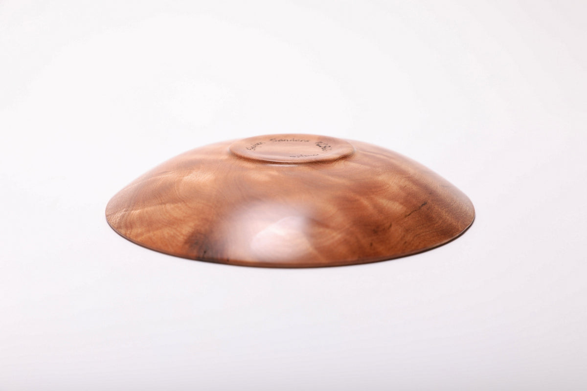Underside of the quilted maple ring dish, showing its curved honey-toned base and small circular foot with handwritten markings.