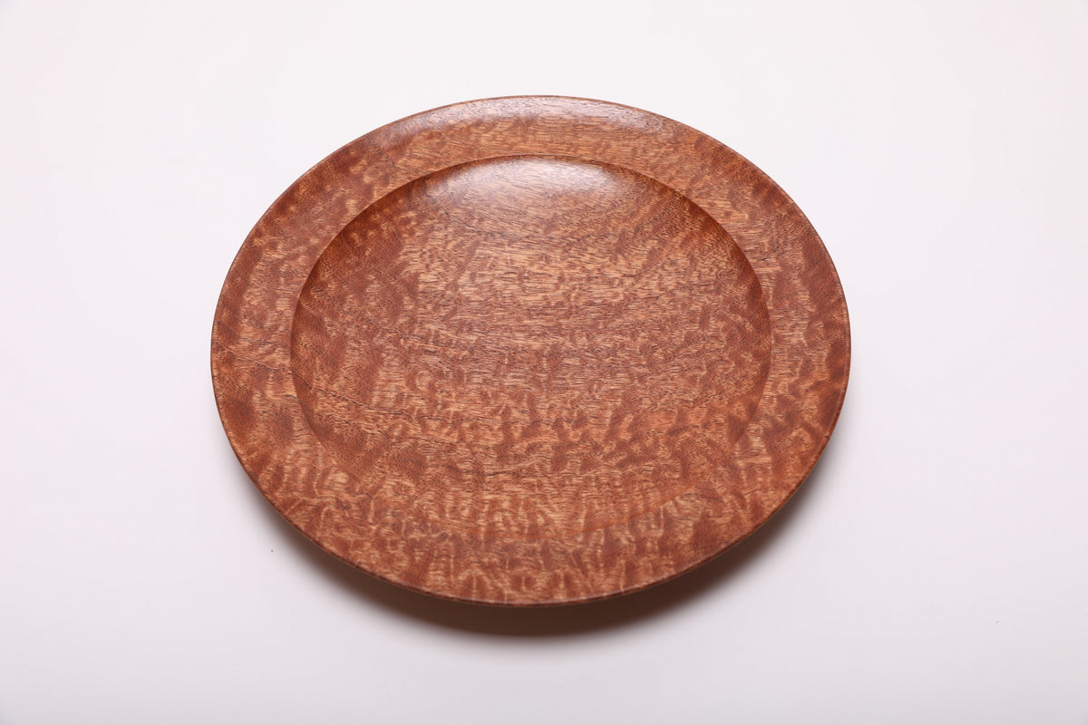 Top view of a shallow pommele sapele wooden bowl with copper-colored dappled figure and a broad curved rim.