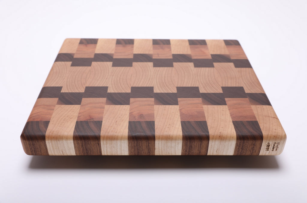 Angled view of the end grain cutting board showing contrasting wood blocks and a small maker’s mark on the front edge.