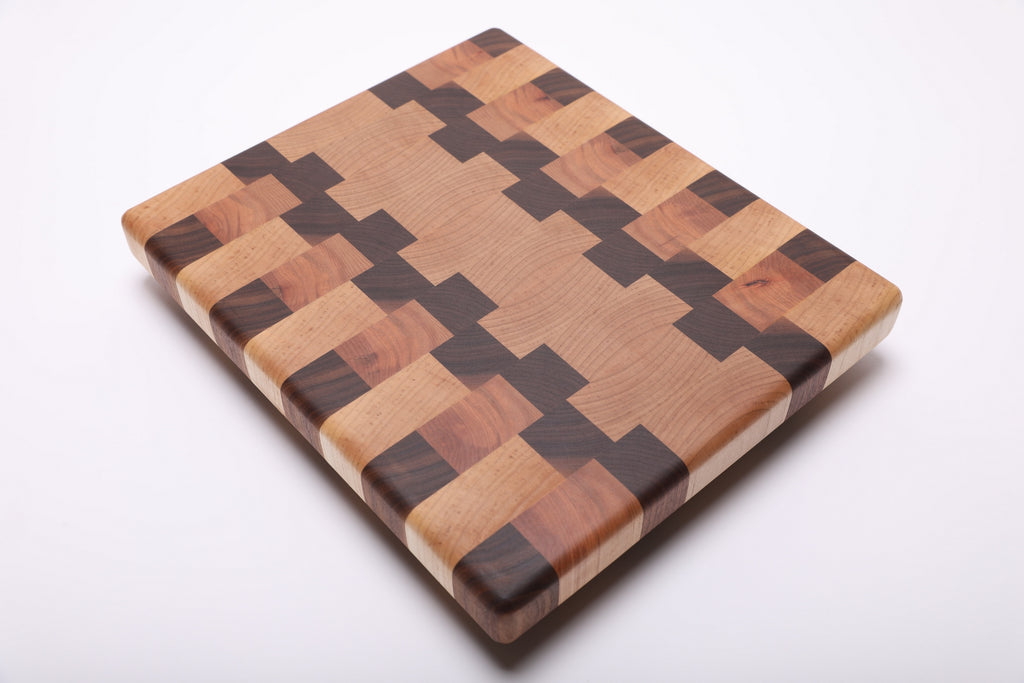 Rotated diagonal view of the cutting board highlighting its interlocking maple, walnut and cherry pattern and rounded edges.