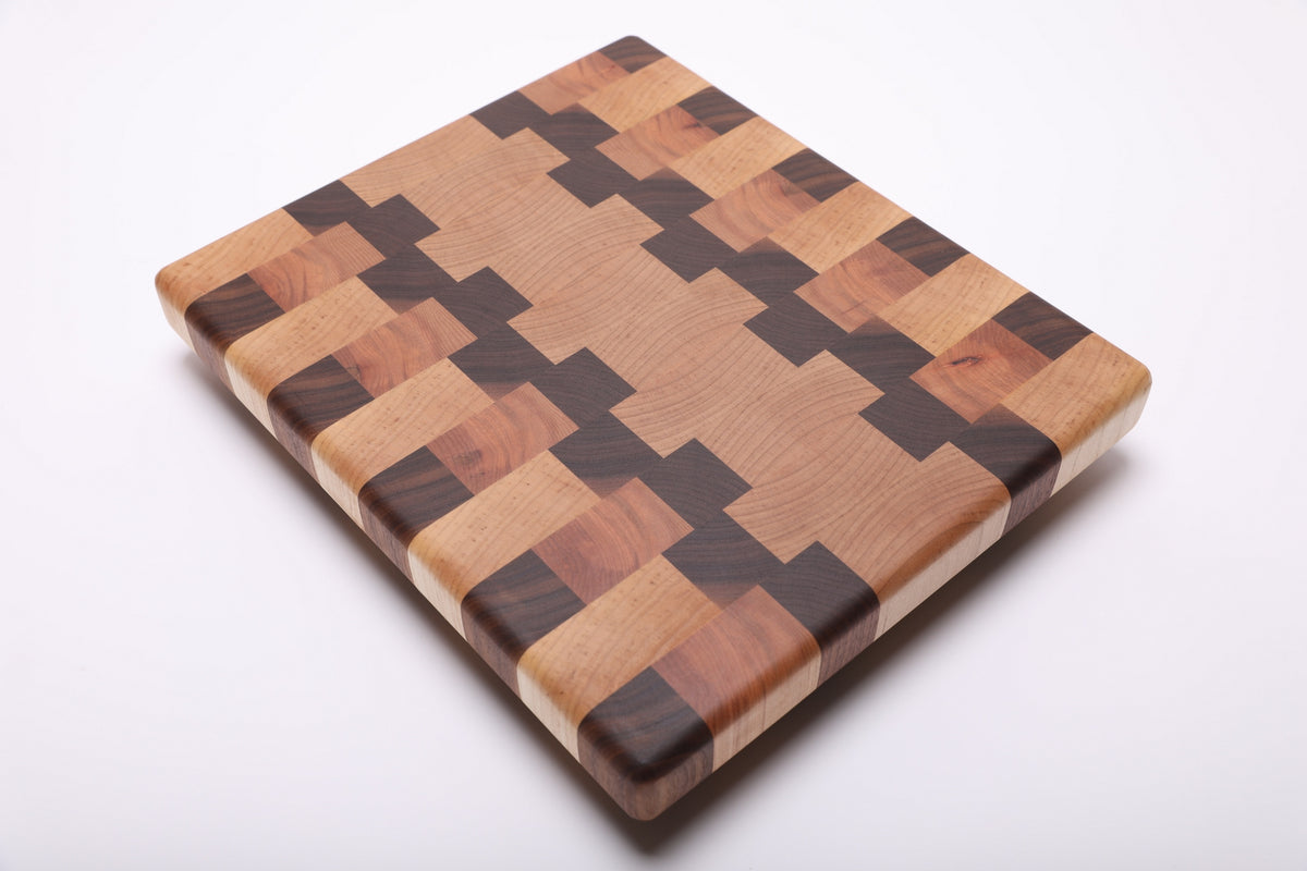 Rotated diagonal view of the cutting board highlighting its interlocking maple, walnut and cherry pattern and rounded edges.