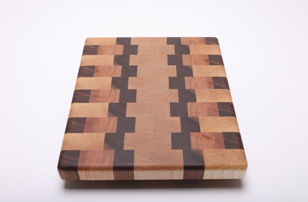 Lengthwise angled view of the end grain cutting board with pale maple, dark walnut and warm reddish cherry blocks.