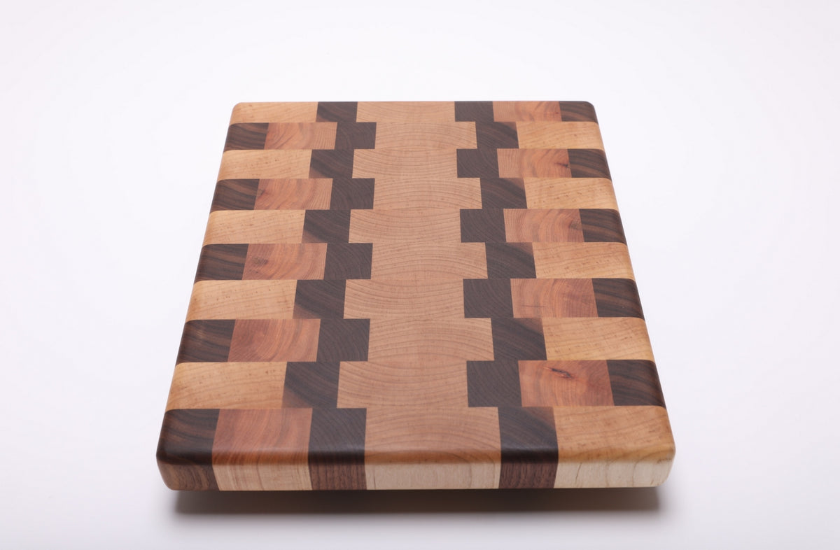Lengthwise angled view of the end grain cutting board with pale maple, dark walnut and warm reddish cherry blocks.